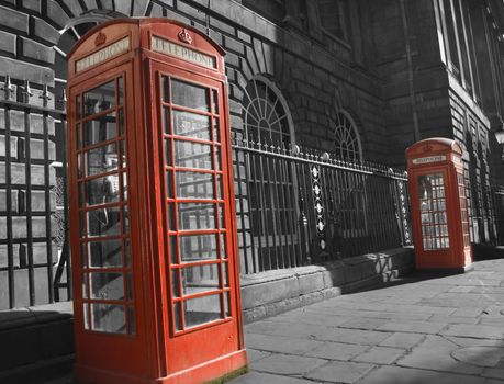 Selective color pair of classic bright red British telephone boxs set against ornate monochrome building