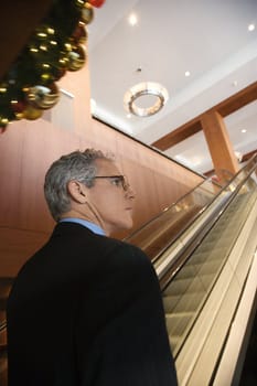 Rear view of prime adult Caucasian man in suit standing on escalator.