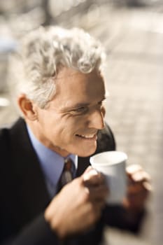 Selective focus close up of prime adult Caucasian man in suit drinking coffee and smiling.