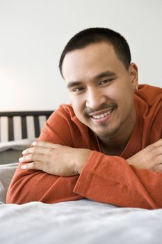 Close-up of Asian young adult man lying on bed looking at viewer smiling.