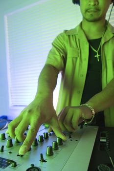 Close-up of Asian young adult male DJ with hand on control panels of mixing equipment.