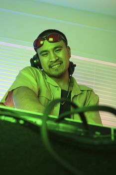 Asian young adult male DJ behind mixing equipment looking at viewer smiling.