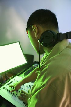 Rear view of Asian young adult male DJ mixing music on equipment.