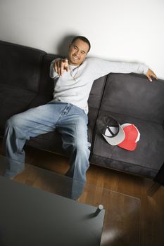 Asian young adult man sitting on sofa smiling and pointing at viewer.
