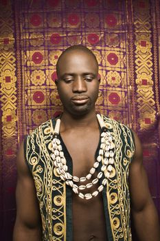 Portrait of African-American mid-adult man wearing embroidered African vest and beads.