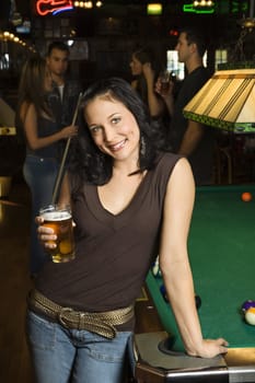 Portrait of young caucasian woman holding beer beside billiards table in pub.