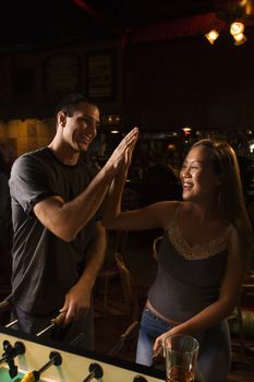 Young couple teamed up at foosball game in pub clasping hands in victory.