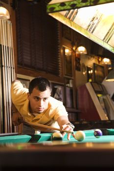 Young man concentrating while aiming at pool ball while playing billiards.