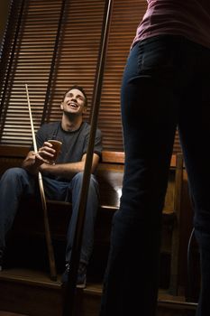 Young man with billiards cue talking with woman standing before him.