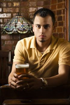 Portrait of serious young Hispanic man holding beer in pub.