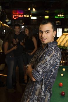 Portrait of smiling young Hispanic man next to billiards table at pub.