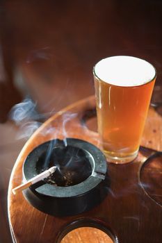 Full beer glass and cigarette with smoke rising in nightclub.