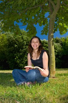 A young girl with a book in a park, smiling.