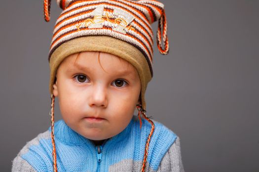 Closeup portrait of a little boy in a nice striped cap, serious thoughtful look