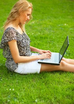 Young woman using her laptop outdoors and sitting on a grass