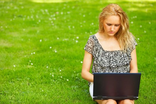 Young woman using her laptop outdoors and sitting on a grass