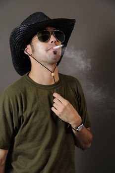 Portrait of young trendy man smoking with cowboy hat