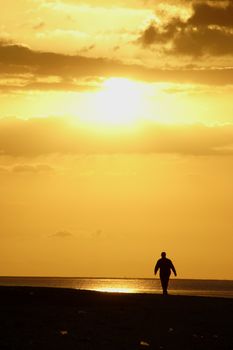 Image of a man taking a stroll on the beach at sunset