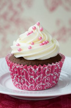 Chocolate cupcake decorated with frosting and pink dragees