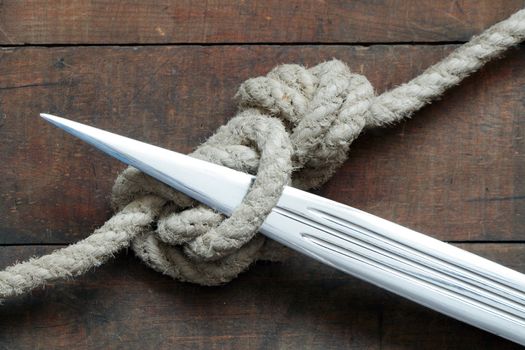 Closeup of dagger and rope tied knot on wooden background