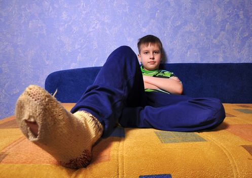 Boy wearing dirty socks with holes in them sits on sofa

