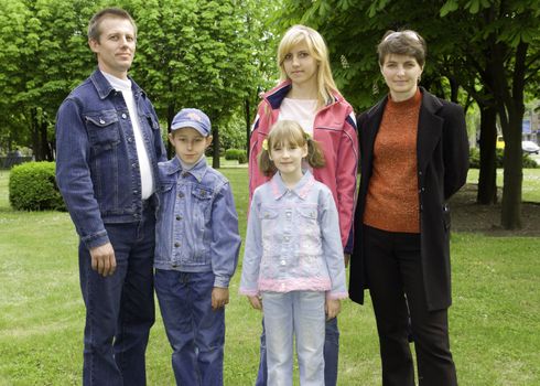 Family with three children on a green grass, against green trees