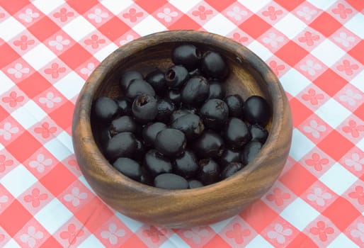a bowlful of preserved black olives on a table cowered with checkered buckram