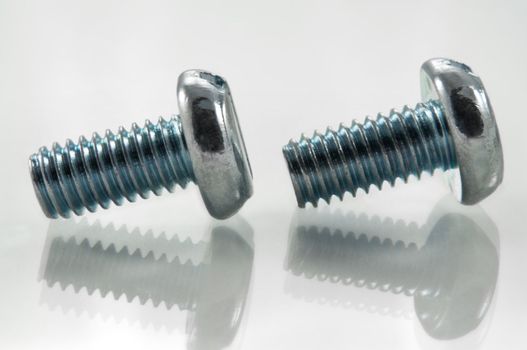 Close, low level capturing two metal bolts on white reflective surface and white background.