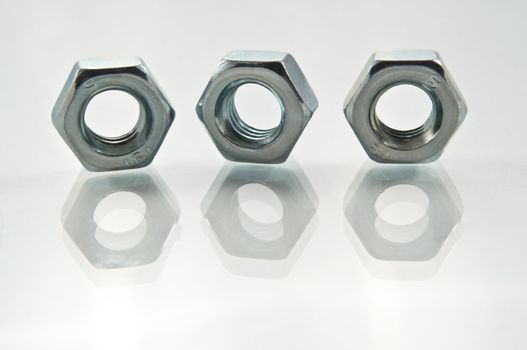 Close, low level of three metal nuts arranged on white reflective surface with white background.