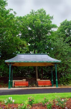 A photograph of a shelter in a park with two wooden benches