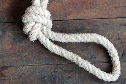 Old thick rope with knot and loop lying on wooden background