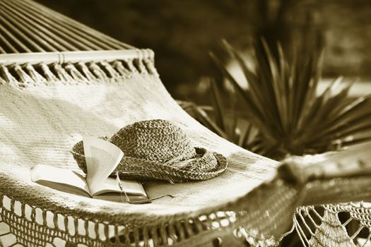 Hammock, book, hat, and glasses on a sunny summer day/ Sepia tone