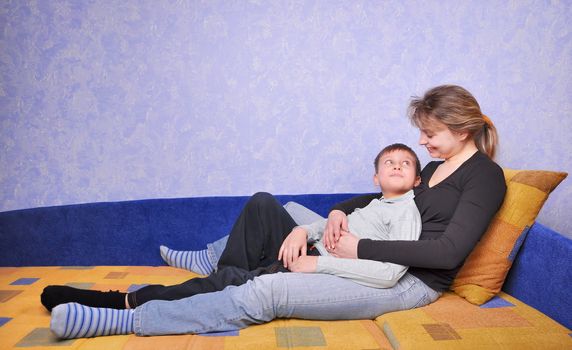 smiling woman and teen boy sits on sofa at home