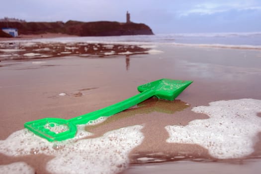 green plastic spade lying on a beach in ireland with ballybunion castle in background as if building a sand castle