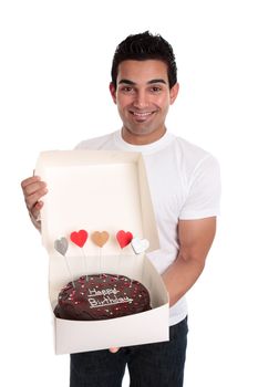 A smiling man holds a chocolate birthday cake decorated with love hearts in a cake box 