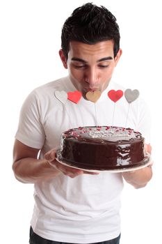 A man kisses one of the heart decorations on a chocolate cake.