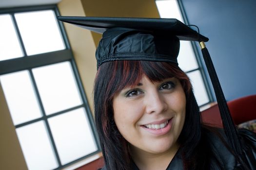 A recent school graduate posing in her cap and gown indoors.