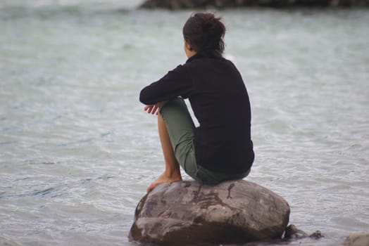 Young woman contemplating on a rock by a river