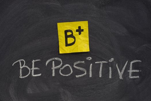 B+, be positive concept, yellow sticky note and white chalk handwriting on blackboard