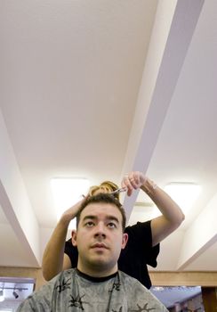 A young man getting his hair cut by a hairdresser at the beauty salon.  Plenty of copy space with this unique perspective.
