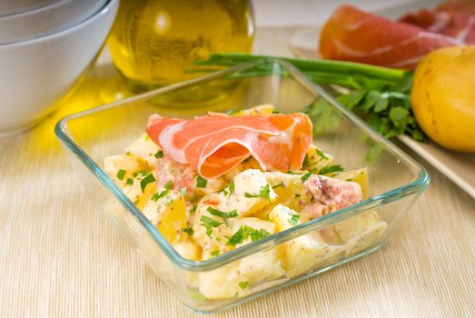 fresh home made parma ham and potato salad,with raw ingredients around with bowls and dishware on a table