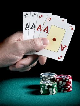 A man's hand holding four aces over three piles of different colors chips on a green felt.