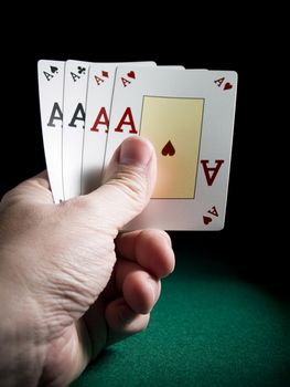 A man's hand holding four aces over a green felt.