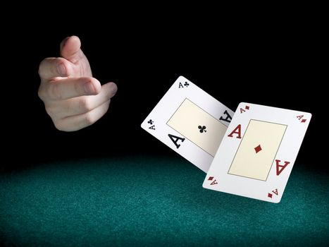 A man's hand throwing two aces over a green felt.