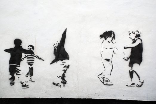 A photograph of a public wall with stencils of children playing in black