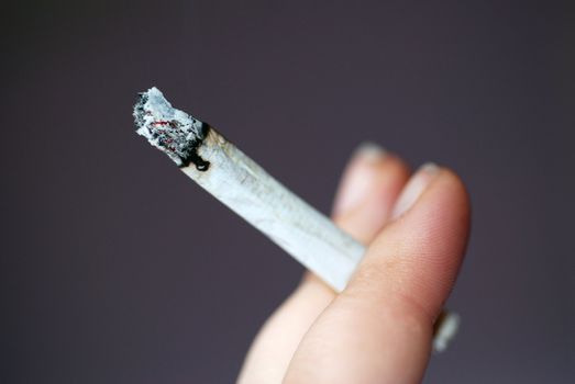 A photograph of a hand holding a roll-up cigarette or joint.