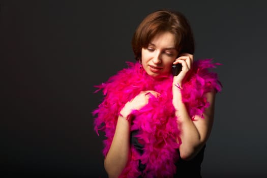 Beautiful woman in pink feathers speaks on phone. Close-up view