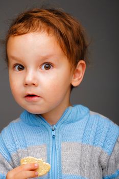 Portrait of a suprised little boy in a blue sweater with a cookie