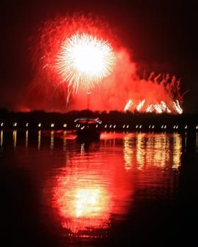 Fireworks with reflections in a lake and a boat.