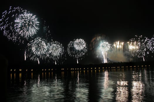 Long line of white or silver fireworks with reflections in a lake.